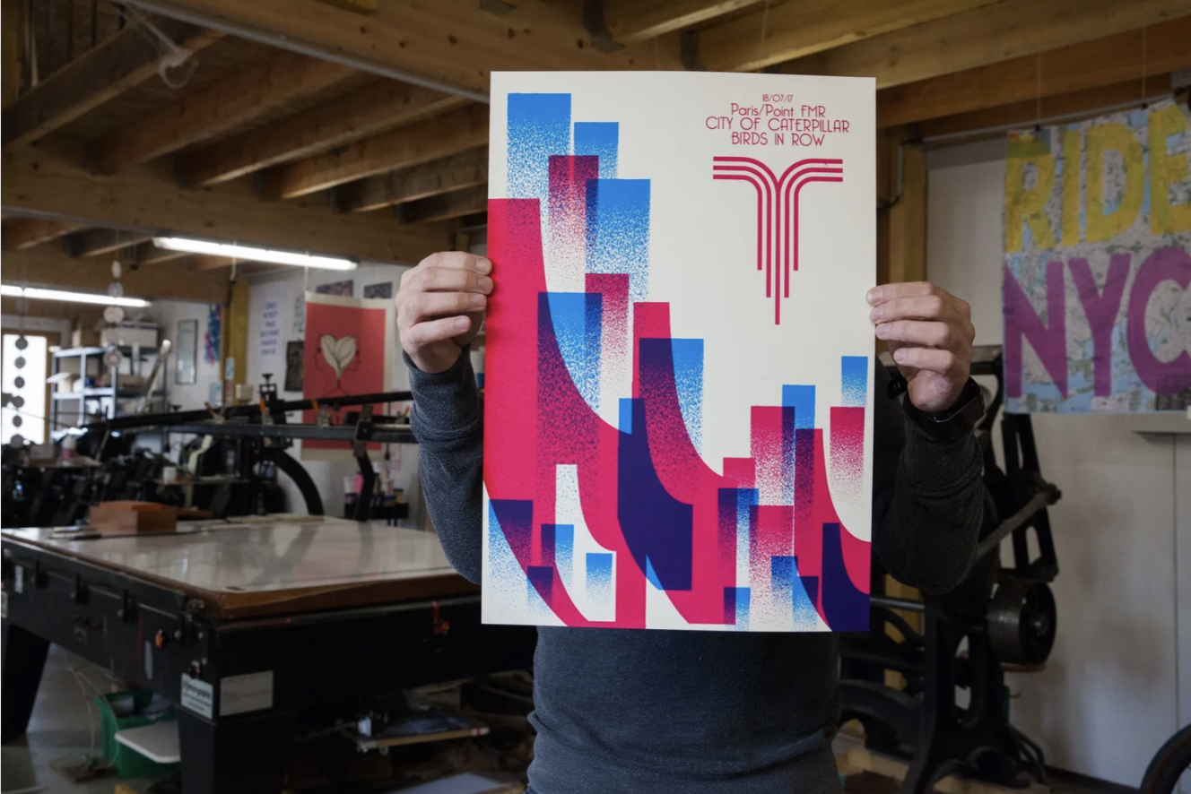 BrianCougar tenant une affiche sérigraphiée dans son atelier
